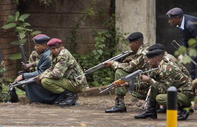 Armed police from the General Service Unit take cover behind a wall during a bout of gunfire, outside the Westgate Mall in Nairobi, Kenya, on Monday, where terrorists are holding an unspecified number of people hostage.AP