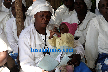 A woman reading a hymn book with a baby on her laps during the Anglican church blousing ceremony in Lusaka west