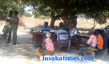 Police officers attending to members of the public under a tree because there is no infrastructure in Garnaton area of Kitwe town