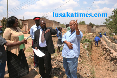 Lusaka District commissioner Christah Kalulu(left)looks on as Lusaka Province Permanent Secretary Stephen Bwalya(middle)and Mtendere ward 32 councillor,James Maimba pointing to and area where the drainage system is being done during the tour of drainage clearence in Mtendere compound