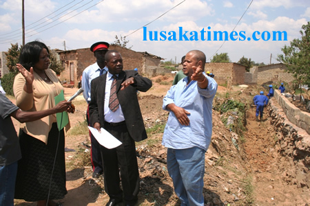 Lusaka District commissioner Christah Kalulu(left)looks on as Lusaka Province Permanent Secretary Stephen Bwalya(middle)and Mtendere ward 32 councillor,James Maimba pointing to and area where the drainage system is being done during the tour of drainage clearence in Mtendere compound