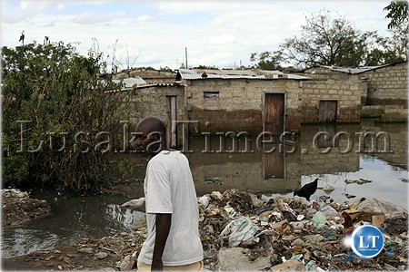 Continuity or change?-An unidentified man walks past gabbage and flooded houses in Chawama