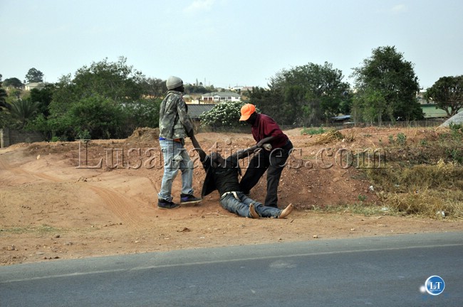A passerby helps a Lusaka youth lift an intoxicated colleague along Ibex Hills road on Independence Day