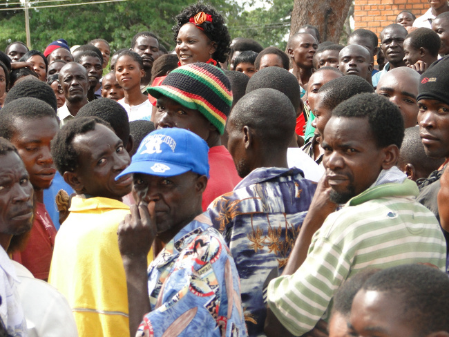 Chinsali district commissioner (DC) Evelyn Kangwa (in the centre with a read ribbon in the head) mobbed by hundreds of job seekers who stormed her office demanding to know when the construction works at the new provincial administration site in the district would commence so that they can be employed