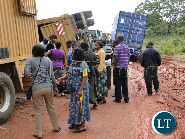 Several passengers on the Lusaka and Copperbelt bound buses where yesterday stranded for sometime near Kafwimbi primary school in Isoka district along the Great North Road in Muchinga Province after two trucks and trailers collided head-on and flipped on one side blocking the road. In the picture, stranded passengers looking at the two trucks and trailers which flipped on one side after colliding head-on.Occupants from both trucks escaped unhurt