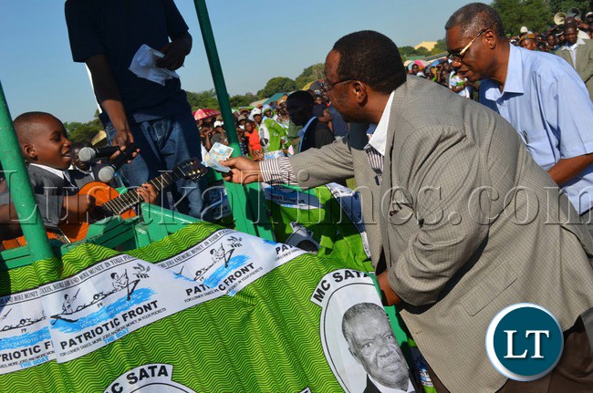 Cabinet Ministers Emmanuel Chenda (right) and Geoffrey Mwamba (left) gives 10 year old Livingstone guitarist and singer Mordecai Munjoma, who is also a recent winner of the Talent Yapa Zed