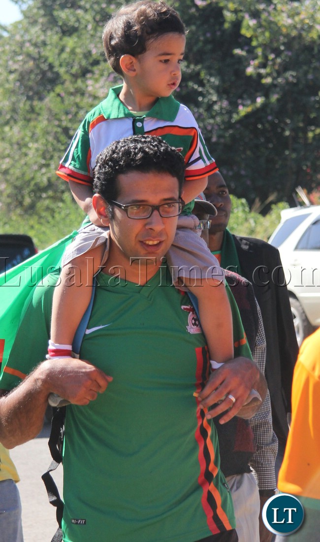 A chipolopolo fan makes his way to the stadium as his son enjoys the ride on his shoulders