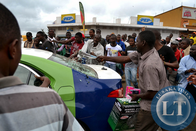 The angry mob smashes the rear wind shield of the patrol car in the confusion that ensued