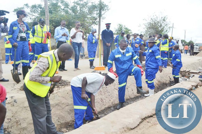 Lusaka Province Permanent Secretary Wamunyima Muwana (with raised leg), Lusaka District Commissioner Ashell Kampengele ( wearing hat) and Chawama Ward two councilor Potipher Tembo (in grey trousers) when they joined female Road Development Agency female members of staff to clean drainage facilities in Chawama Township ahead of International Women's Day
