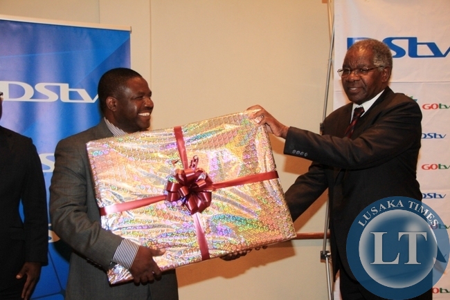 Chairman of MultiChoice Zambia Dr John Mulwila SC presents a present to the out-going Director General of Zambia National Broadcasting Corporation (ZNBC) Chibamba Kanyama at his farewell cocktail party hosted at Lusaka’s Pamodzi Hotel as MultiChoice acting public relations manager Mumbi Mutale looks on.
