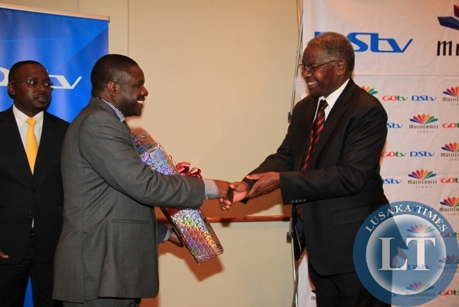 Chairman of MultiChoice Zambia Dr John Mulwila SC presents a present to the out-going Director General of Zambia National Broadcasting Corporation (ZNBC) Chibamba Kanyama at his farewell cocktail party hosted at Lusaka’s Pamodzi Hotel as MultiChoice acting public relations manager Mumbi Mutale looks on.