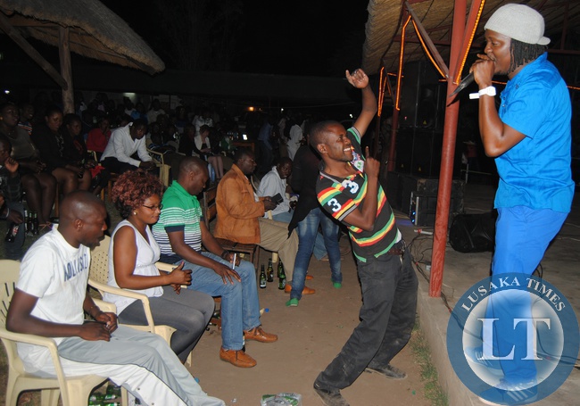 Danny Kaya (in blue) performs on the stage with his live band joined by a fan in Choma on