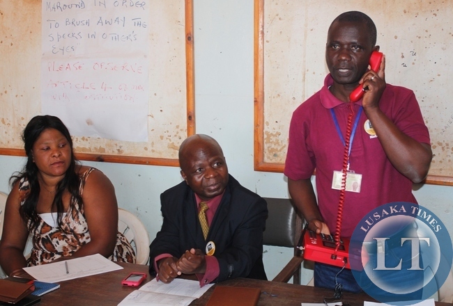 Mbala District Information Officer, Aston Nyungwe (standing right) explaining to the beneficiaries how the community payphone provided by government throuth ZICTA works