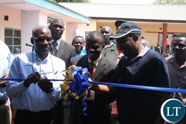 Solwezi acting district commissioner Chipawa Chipawa (m) with chief Mumena (right in a cap) and Lumwana mining company community relations superintendent Harrington Kanema (l) cutting a ribbon during the official handover of Mukamena Multipurpose cooperative centre which has been constructed by Lumwana mining company at Mutanda at a total cost of K240,000