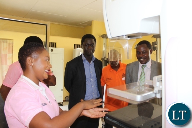 Lewanika General Hospital Radiographer Technologist Angelica Mwaba (l) demonstrating how the breast cancer screening is done on a Mammography Machine as Western Province Assistant Secretary Sineva Kambenja (r) and Provincial Medical Officer Dr. Andrew Silumesii (c) observe during the Breast Cancer Awareness Month Commemoration at Lewanika General Hospital in Mongu
