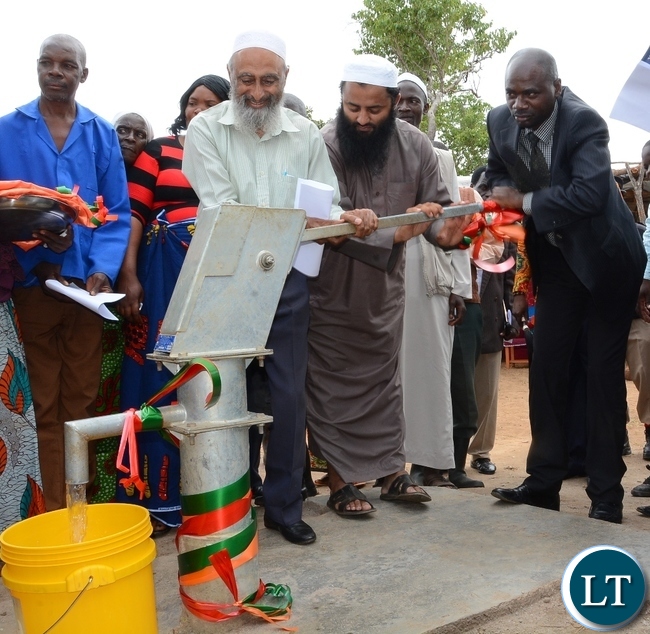 Chisamba District Commissioner Martin Chowa(l),Muslim Social and Welfare Trust coordinator Mubasshir Mehta (c) and Muslim Social and Welfare Trust Representative Haroon Ghumra(r) demonstrating how to use the borehole to the people of Mpikwa Village immediately after donating it to the people of Mpikwa Village in Chisamba District