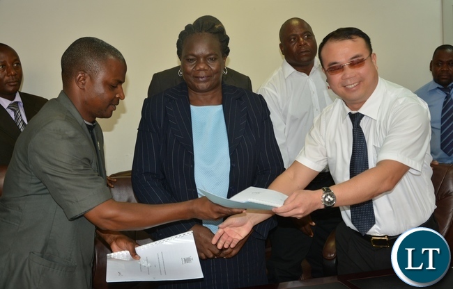 Secretary General of the Public and private bus drivers Associations of Zambia Mr Majuru shake hands with General of the Public and private bus drivers Associations of Zambia Wu Ming while Permanent Secretary of the Ministry of Youth Sport and Child Development Ms Agnes M Musunga looks during the singing of the memorandum of implementation of the empowerment scheme for the youth bus drivers with