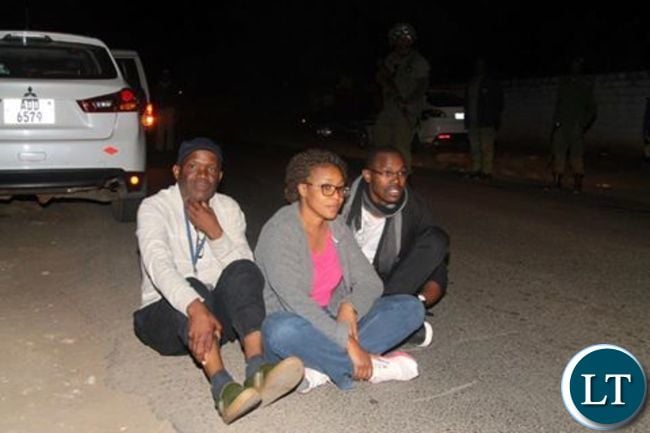 Fred Mmembe with wife Mutinta and Joseph Mwenda sit outside Bwinjimfumu road after they were arrested