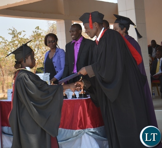 Zambia News and Information Officer (ZANIS) Livingstone Information Officer Angela Mwandu (left) receiving her Bachelor of Arts Degree in Journalism and Communication from Rusangu University Chancellor Samuel Sinyangwe (right) during the 10th Graduation Ceremony for Rusangu University in Monze