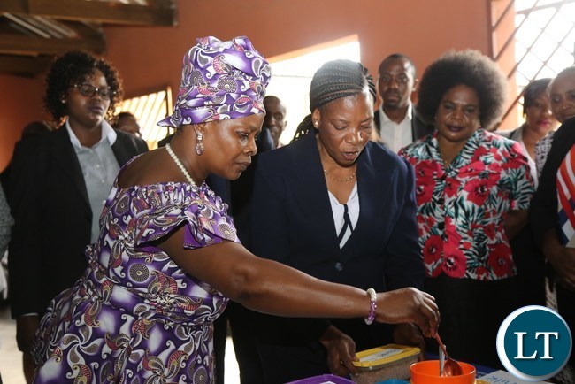 First Lady Esther Lungu flanked by Misissi Outreach Health Centre Nutritionist Lina Sianzele(r) samples some food stuffs during the hand over of food hampers to beneficiaries of Misissi Health Outreach Center at St.Lawrence Parish in Kamwala South.