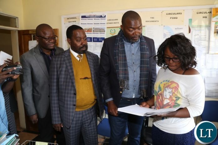 Lusaka Province Minister Bowman Lusambo (c)flanked by Kafue District Commissioner Joseph Kamana (L)looks on the log in book during the spot check of some selected government departments in Kafue District