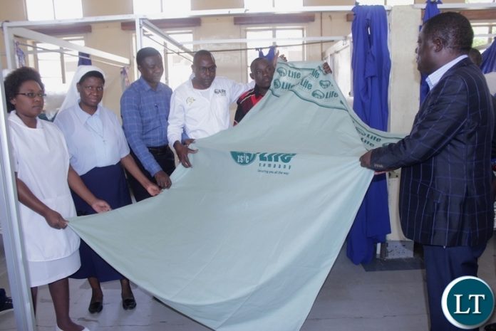 Mongu District Commissioner Susiku Kamona (r) with hospital officials and ZSIC-LIFE official displays a linen during the donation of 40 linen to Lewanika General Hospital by ZSIC-LIFE to celebrate 50 years