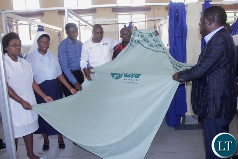 Mongu District Commissioner Susiku Kamona (r) with hospital officials and ZSIC-LIFE official displays a linen during the donation of 40 linen to Lewanika General Hospital by ZSIC-LIFE to celebrate 50 years