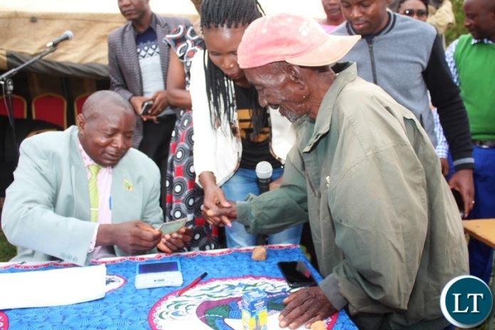 LUNDAZI District Education Board Secretary, Chiza Mtonga, scrutinizes a National Registration Card (NRC) for Bright Nkhata (right) during the payment of Social Cash Transfer funds to beneficiaries at Chipembere Primary School in Lundazi