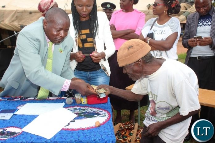LUNDAZI District Education Board Secretary, Chiza Mtonga, hands over money to Whitehead Zulu, during the paymenmt of Social Cash Transfer funds to beneficiaries in Lundazi