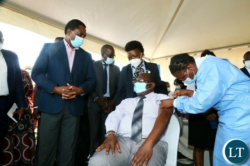 Health Personnel Mutinta Habaalu giving a vaccine ejection to His Royal Highness Senior Chief Luembe whilst President Hakainde Hichilema looks on during the relaunch of COVID-19 vaccine at OYDC