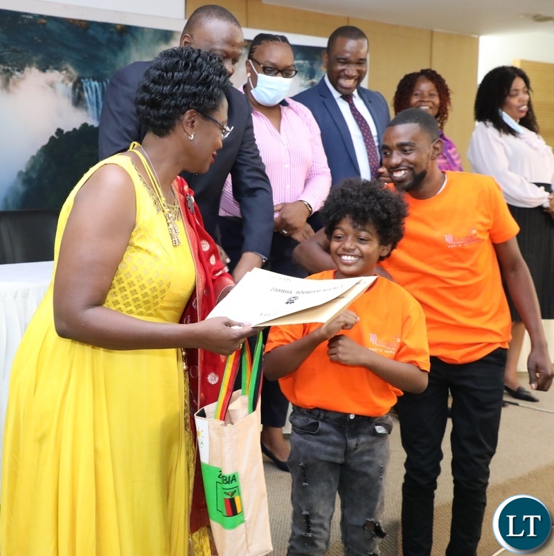 Zambia Tourism Agency Board Chairperson Dr Tecla Ngwenya presents awards to Little Lulu Primary school pupil David Williams as Little Lulu primary school  Teacher Reagan Mwaba looks on  during the Tourism Writing and Arts competition  prize giving ceremony for Primary schools at Government complex  in Lusaka on Monday, October 11,2021 -Picture by THOMAS NSAMA/ZANIS  